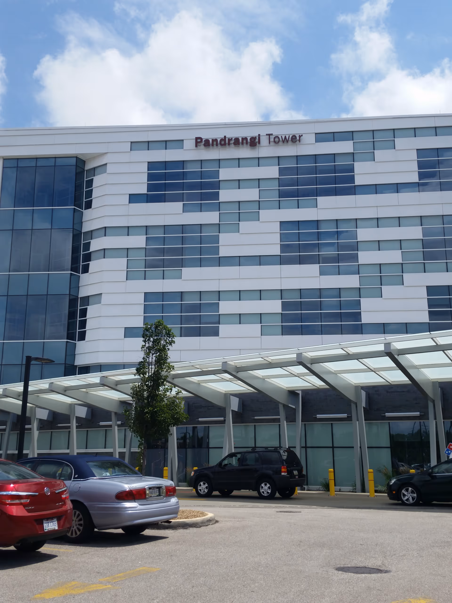 Modern glass-front tower with a parking lot and glass canopy entrance.