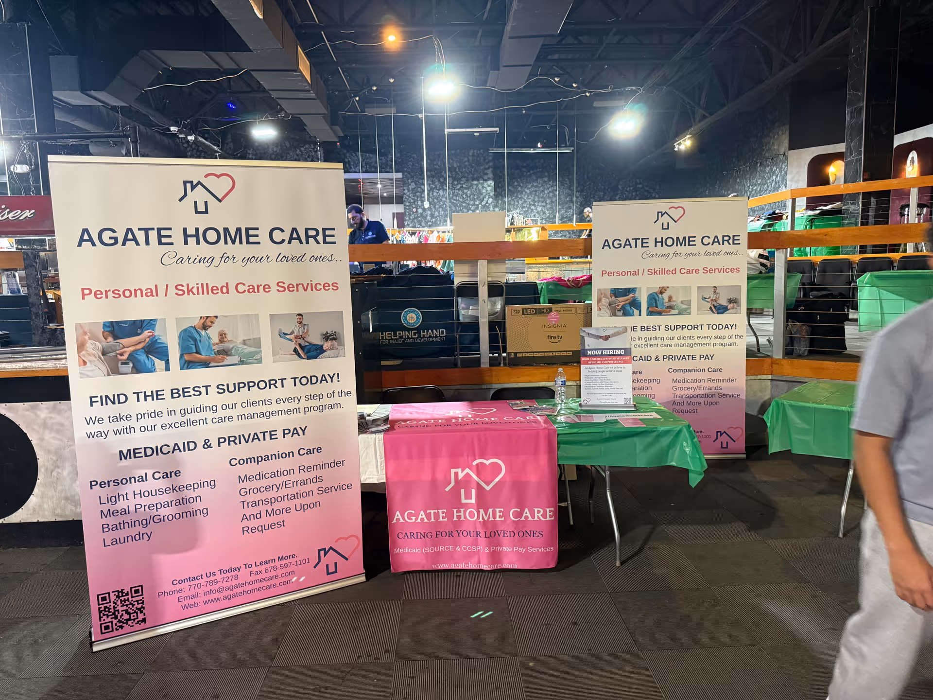 Indoor promotional setup for Agate Home Care featuring banners, tables, and staff signage.
