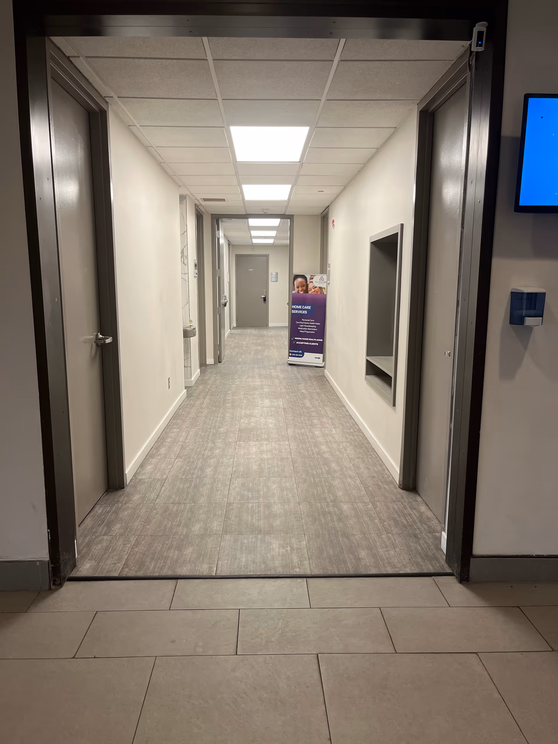 Long, well-lit interior hallway of a senior care facility with doors along both sides.