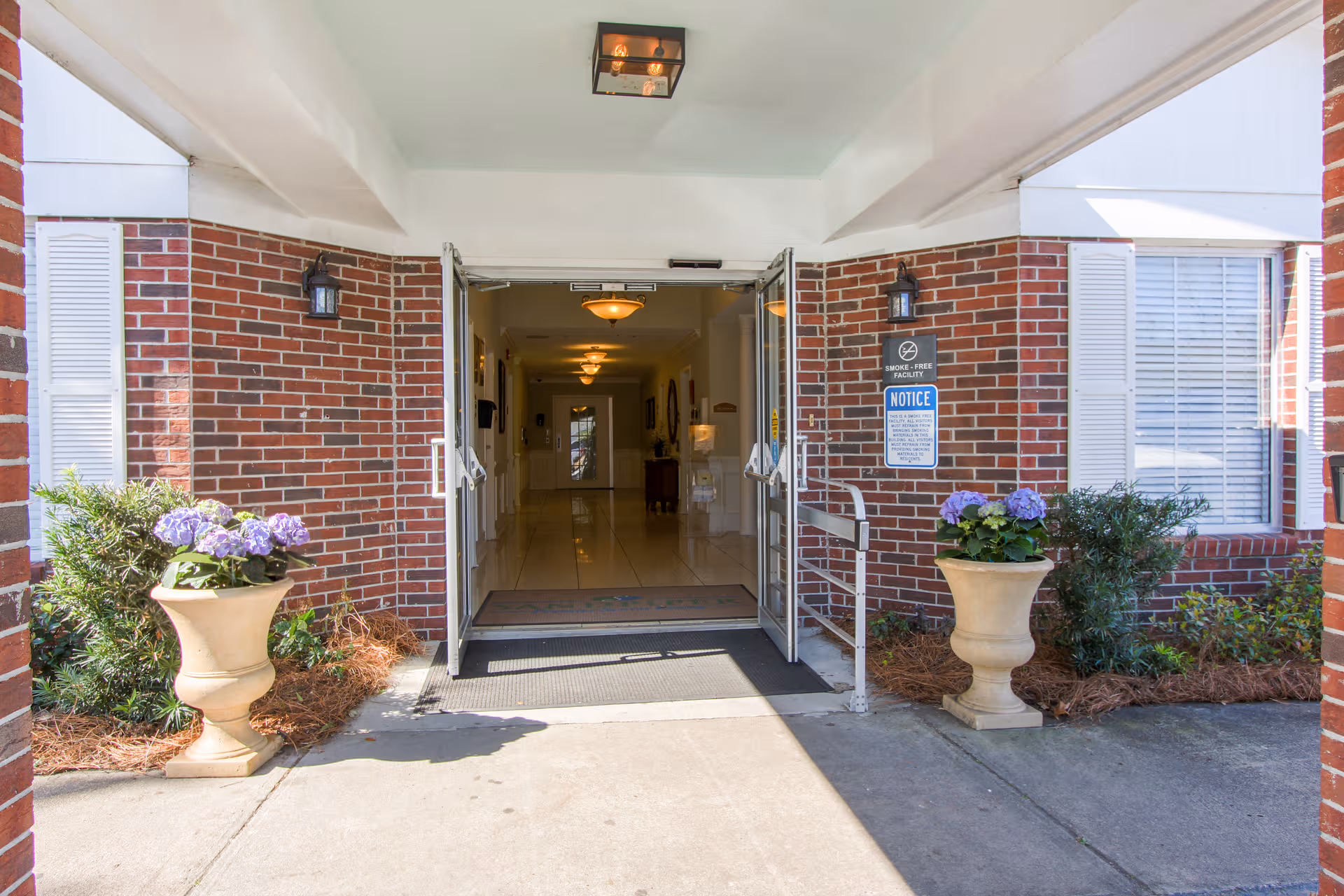 Brick building entrance with open double doors, planters, and lanterns.