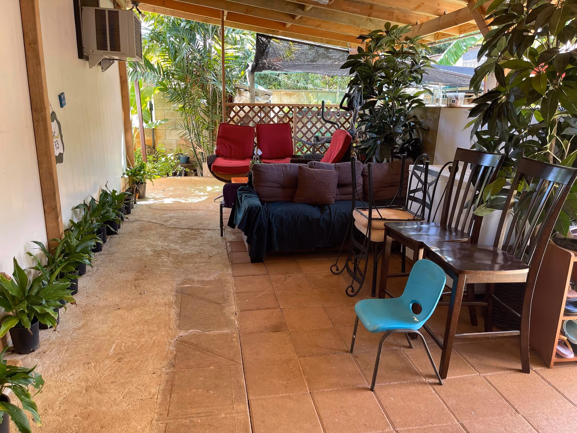 Outdoor covered patio with couches, chairs, and potted plants in a residential setting.