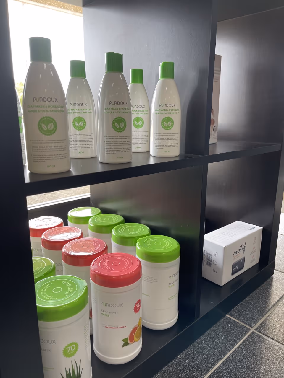 Shelf interior with PURDOUX bottles and wipes arranged on dark display shelves.