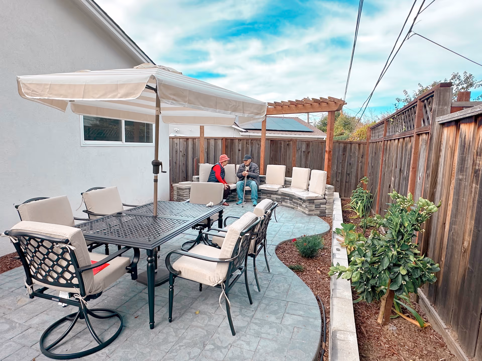 Outdoor courtyard with a dining table, chairs, and two elderly residents conversing.