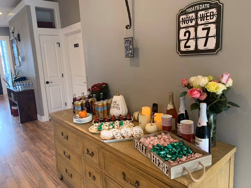 A wooden sideboard along a hallway displays drinks, pastries, candles, and flowers.