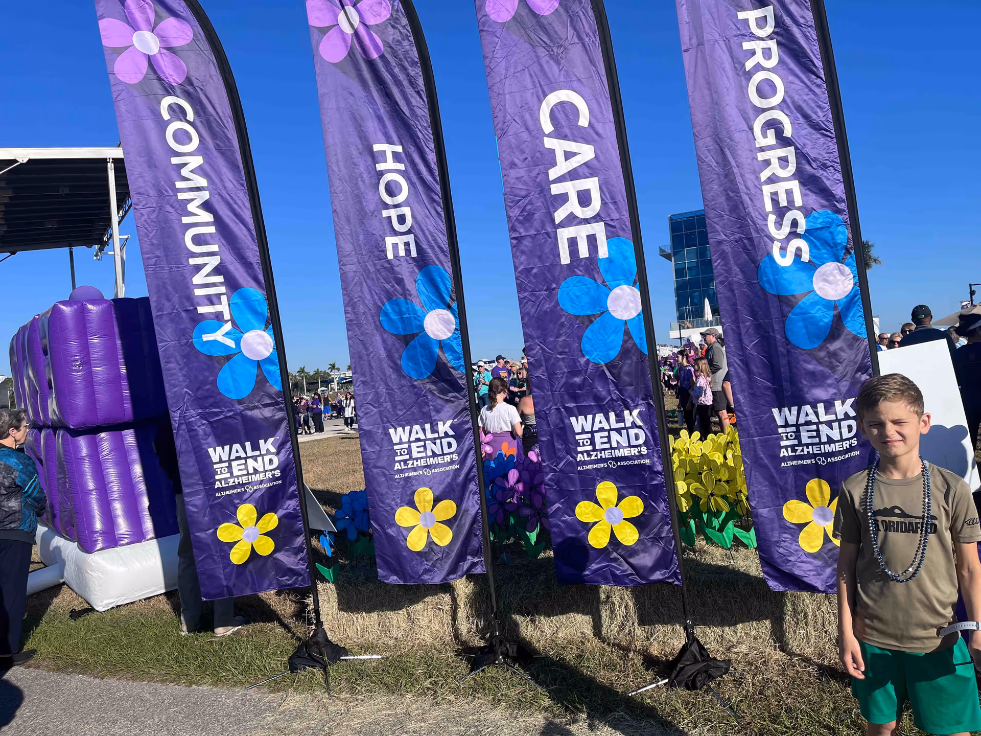 Outdoor event with tall purple banners reading Walk to End Alzheimer's, people gathered on grass.