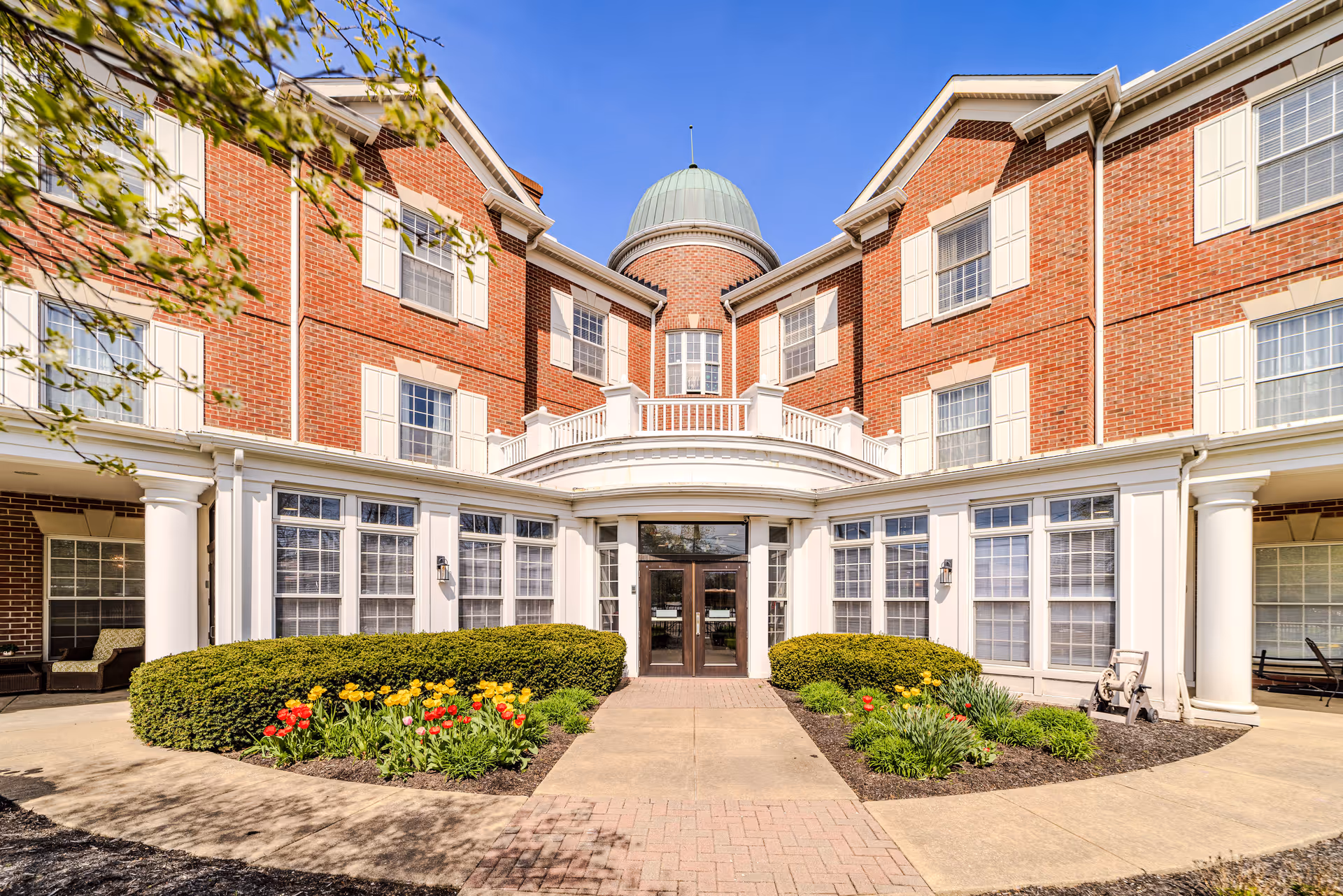 A brick senior living facility with curved entrance and landscaped front walkway
