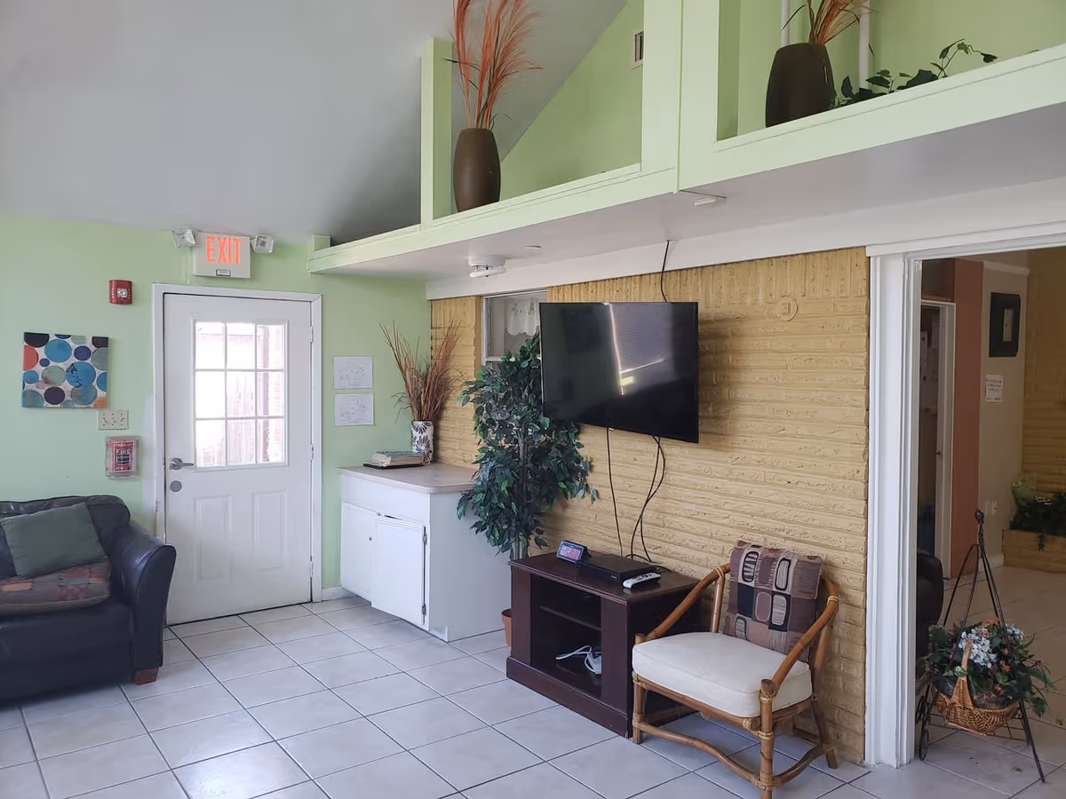 Pastel green lobby-style living area with seating, a wall-mounted TV, and doorway.
