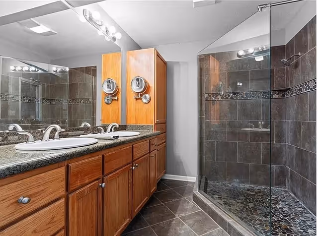 A spacious bathroom with double sinks, wooden cabinets, and a glass-enclosed shower.