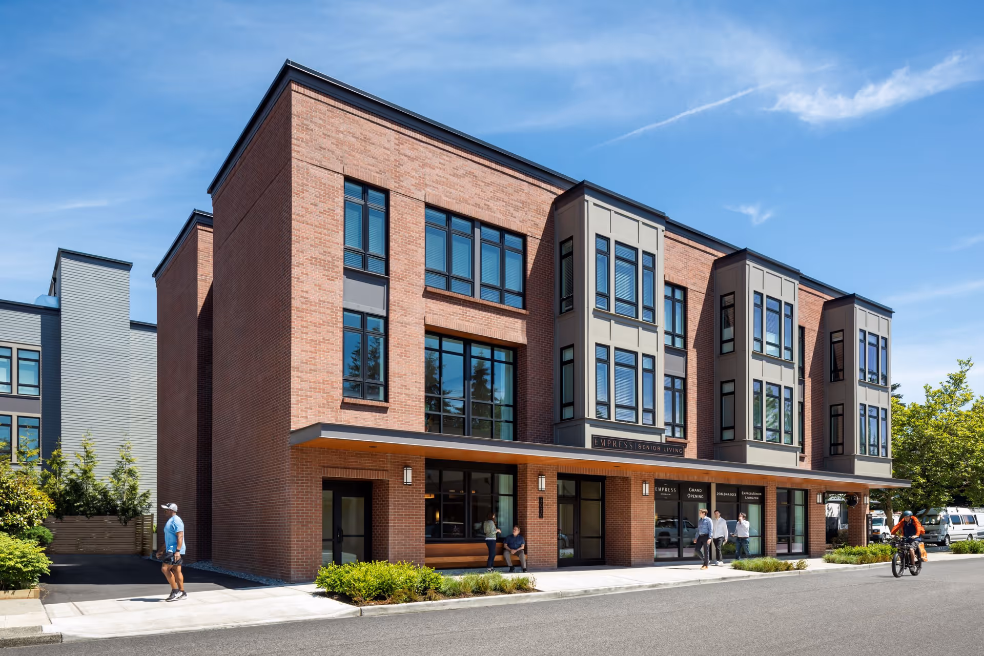 Exterior view of Empress Senior Living at Laurelhurst, brick building with large windows and pedestrians.