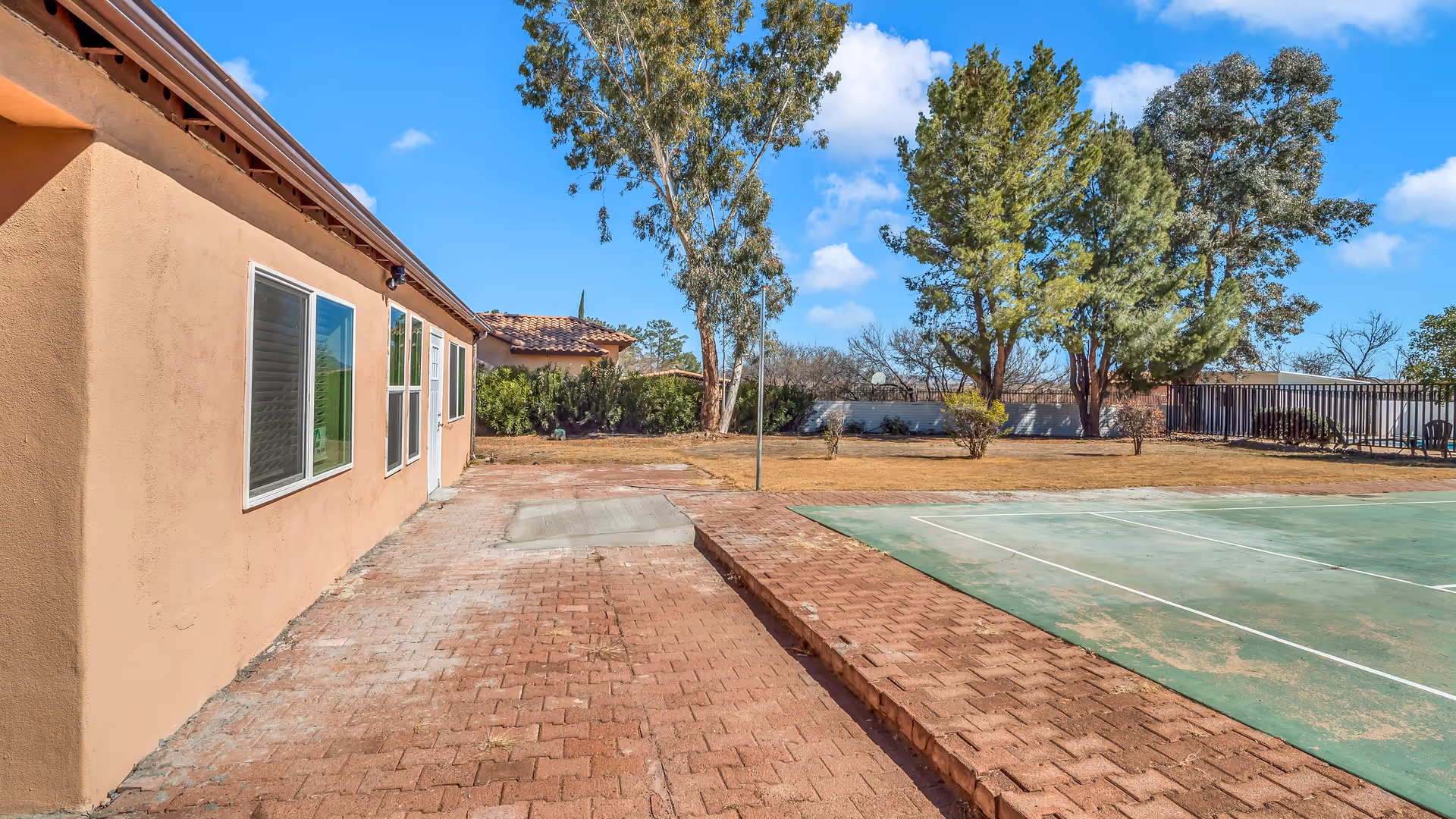 Exterior view of Meadow Hills Assisted Living with brick patio, trees, and a court.