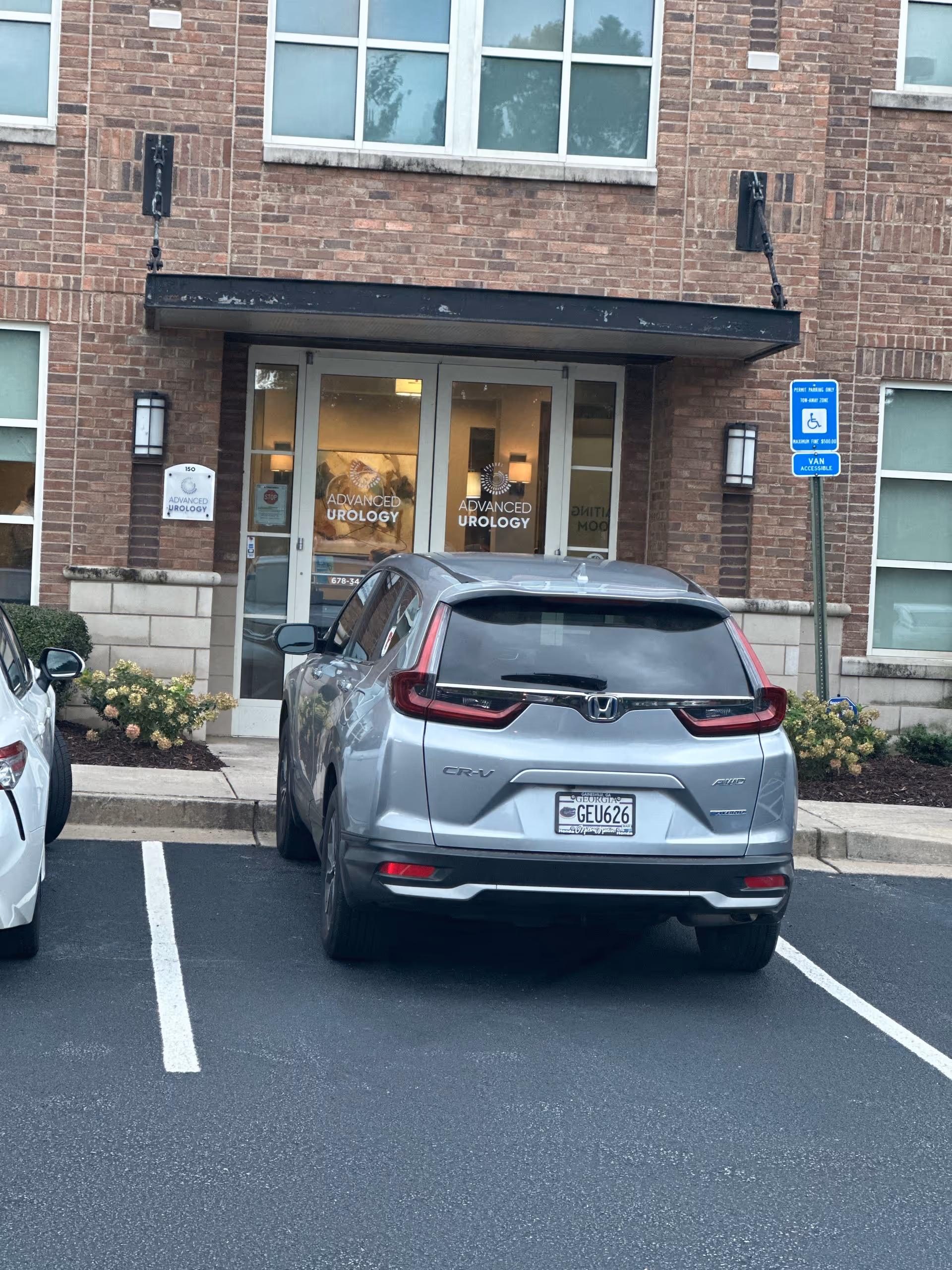 Brick building entrance with double glass doors, Advanced Urology signage, and a parked silver SUV.