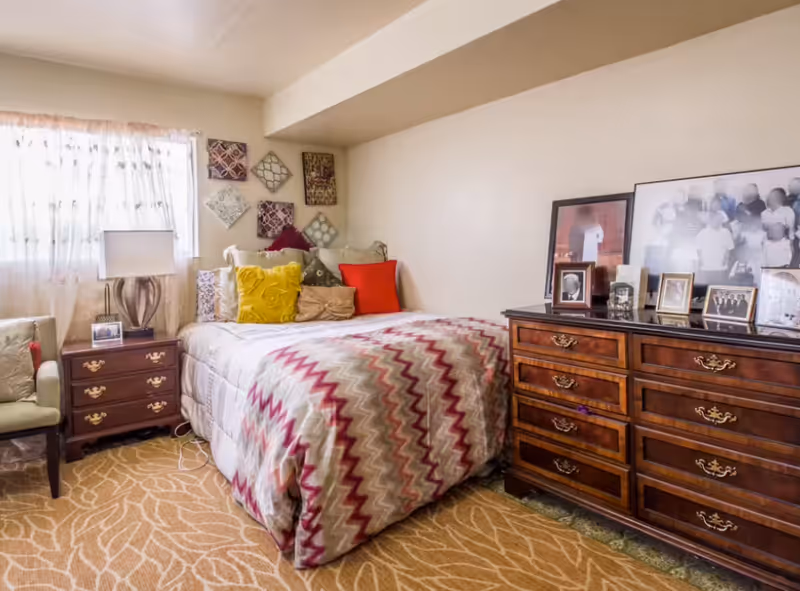 Cozy bedroom featuring a zigzag quilt, colorful pillows, nightstand, and dresser.