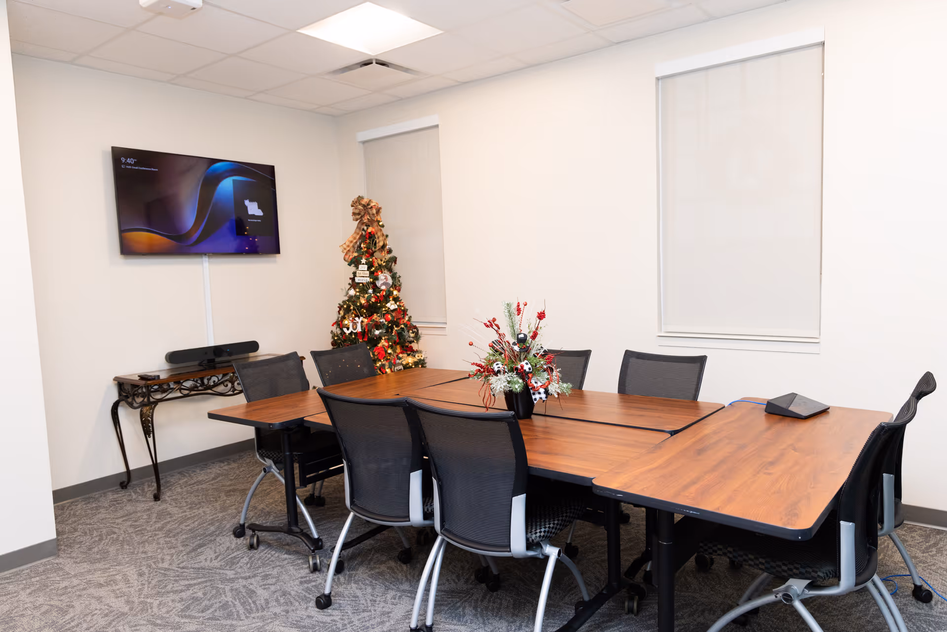 An interior conference room with a large wooden table, chairs, a TV, and a Christmas tree.