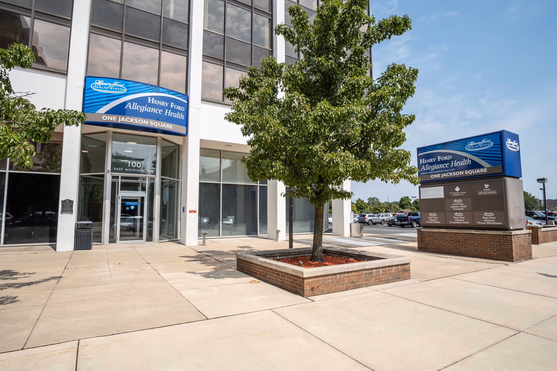 Exterior view of a Henry Ford Allegiance Health facility entrance with a tree and signage.