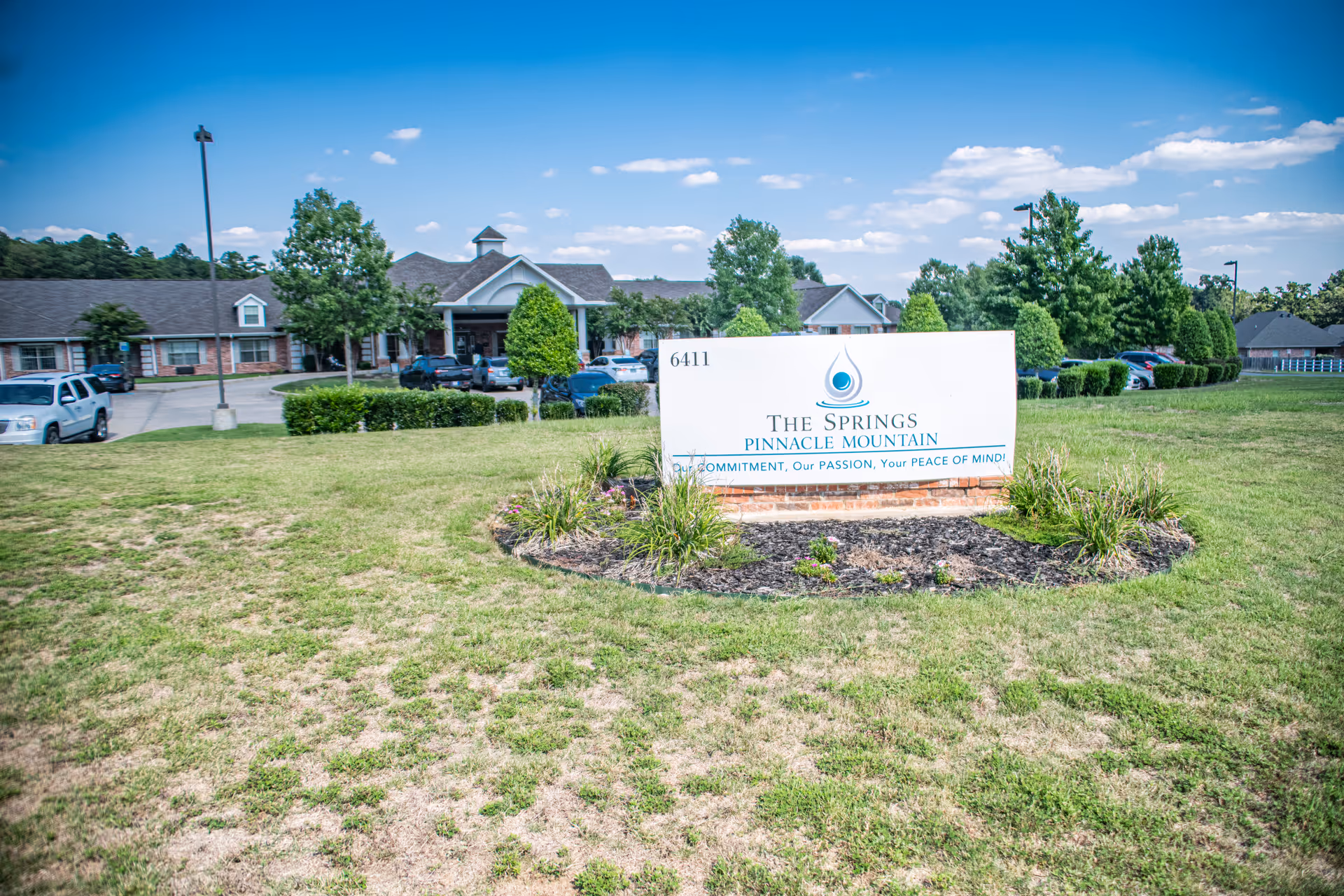 Exterior view of a single-story senior care facility with a front sign on a grassy entrance.