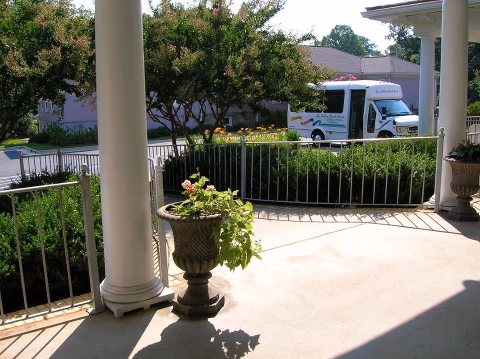 Covered front porch with white columns, planters, and a parked bus in the driveway.