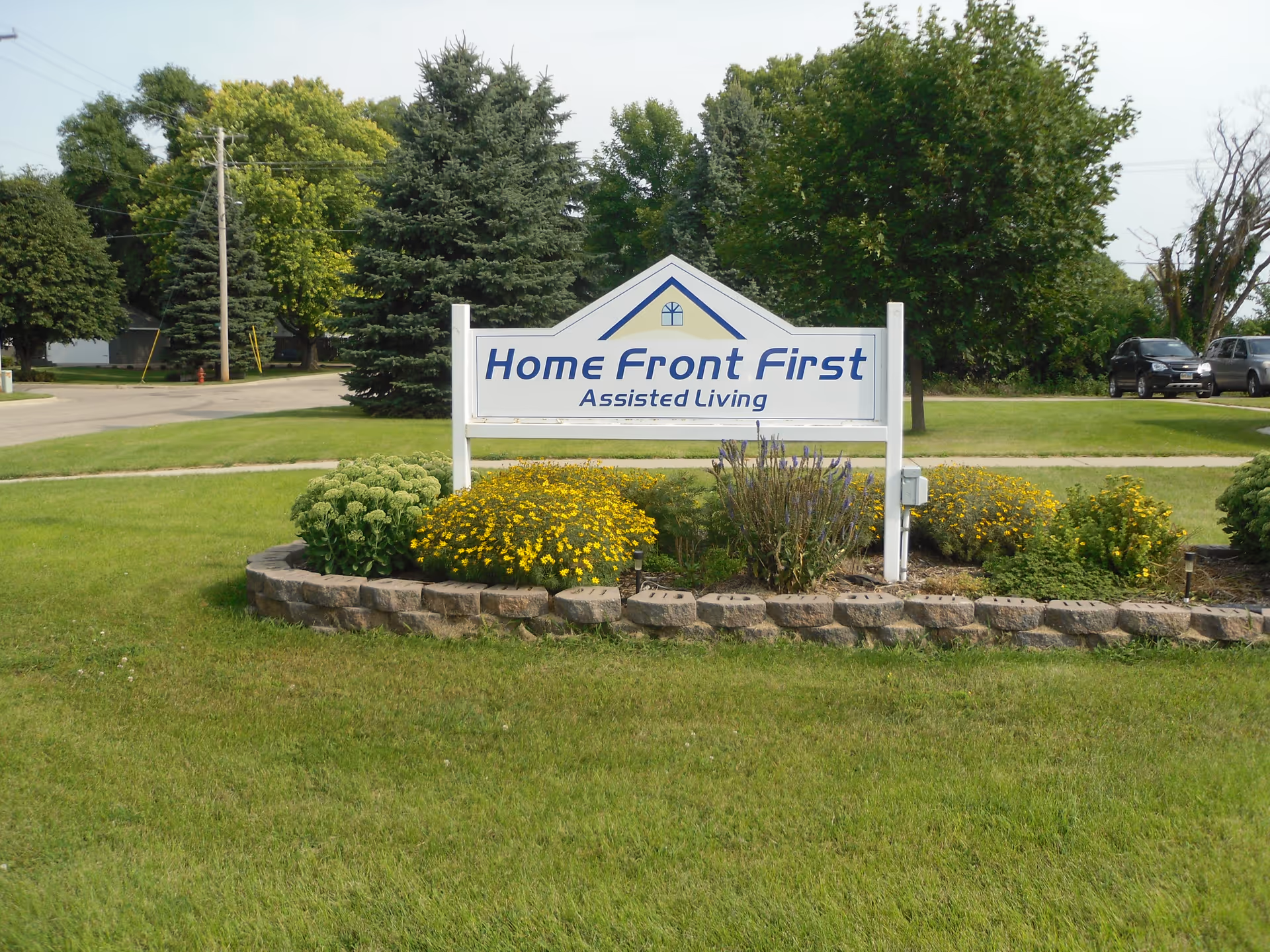 Manicured lawn and flowerbeds frame a sign for Home Front First Assisted Living.