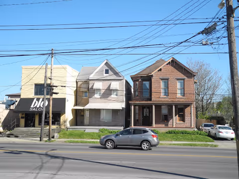 Row of residential buildings along a street with power lines and a parked car.