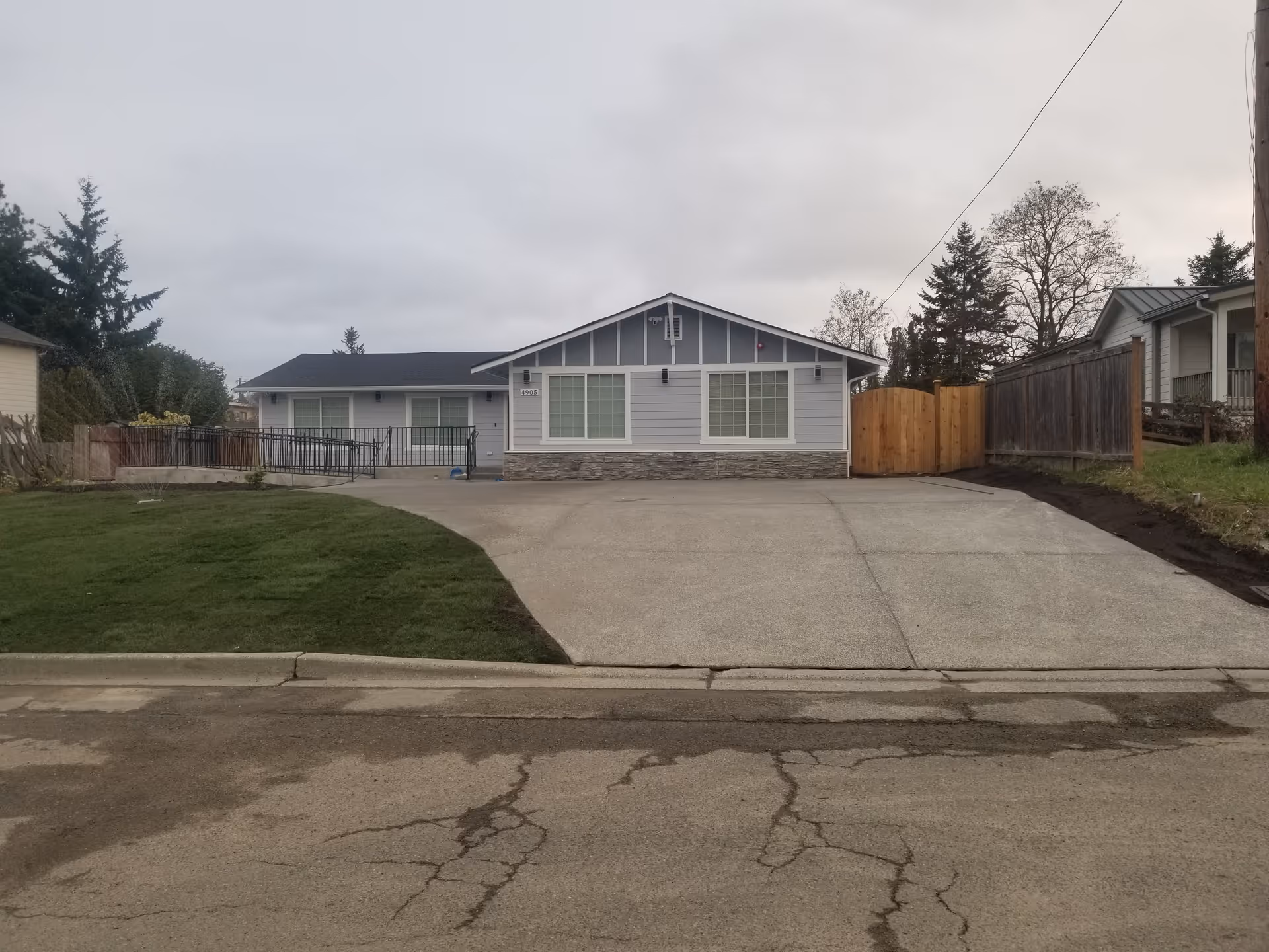 Front exterior of a single-story house with a curved driveway and fenced yard.