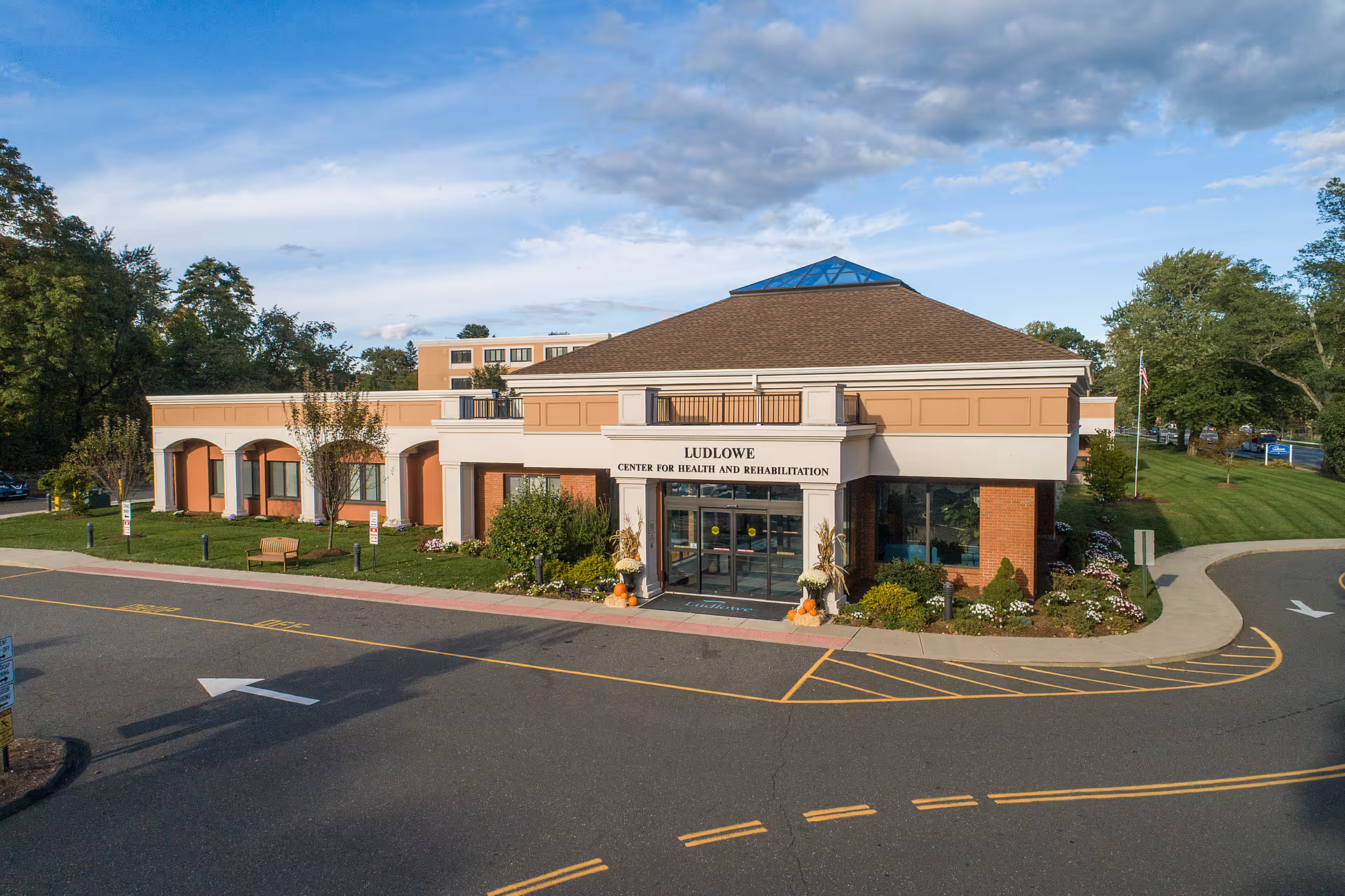 Exterior front view of Ludlowe Center for Health and Rehabilitation building with a driveway and landscaped greenery around the entrance under a partly cloudy sky.