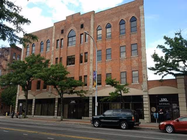 Brick, multi-story building with arched top windows along a city street in Rochester.