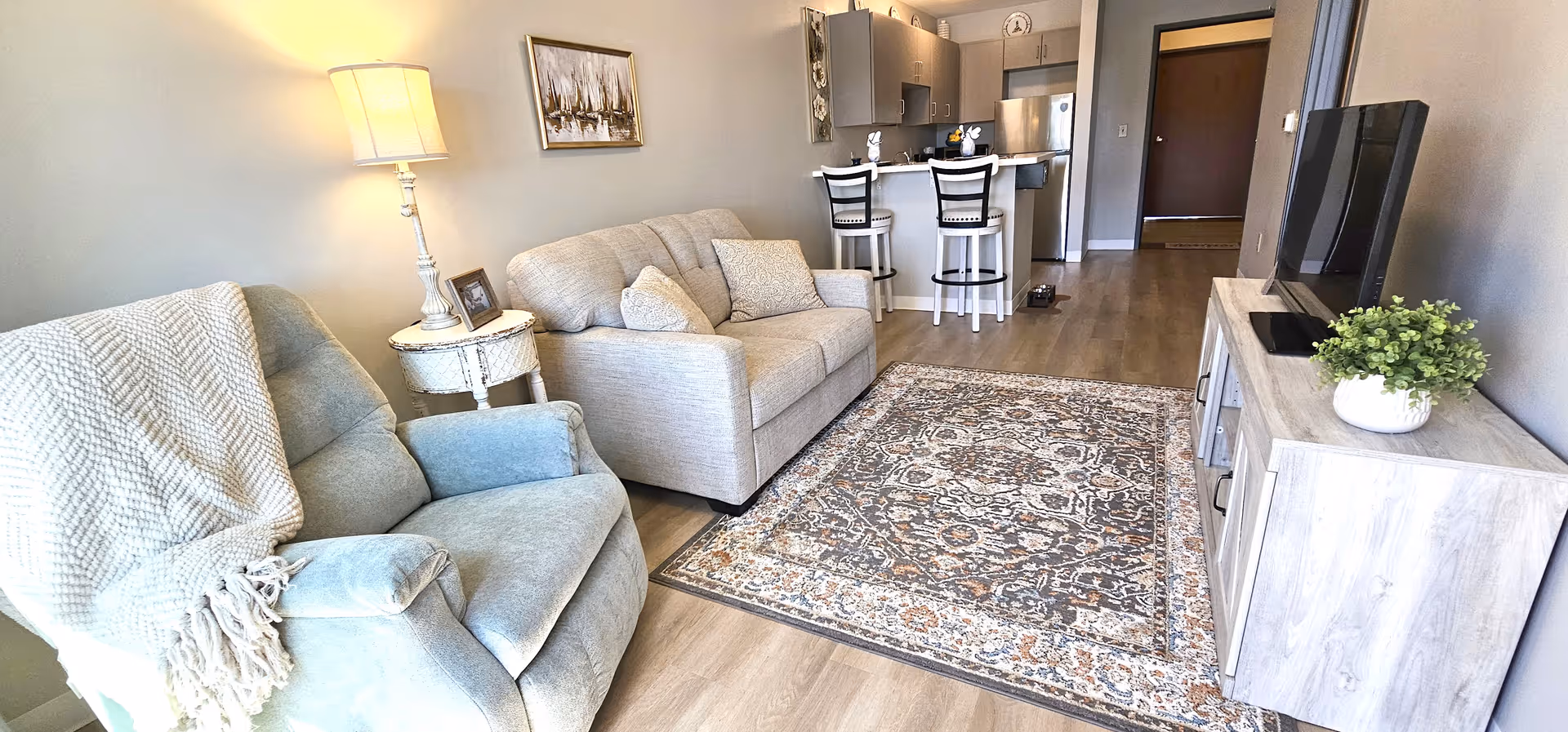 Cozy living room with two sofas, rug, TV, and open kitchen in background.