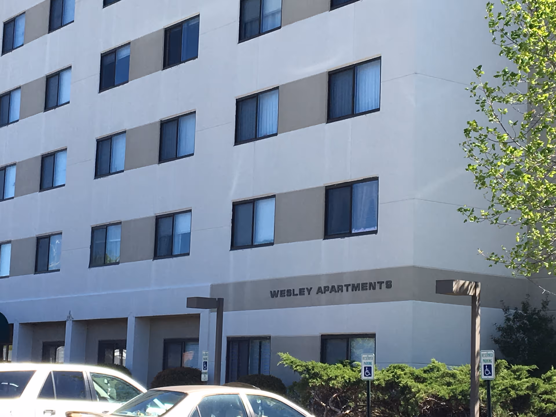 Exterior view of Wesley Apartments building with windows, entrance, and parked cars.