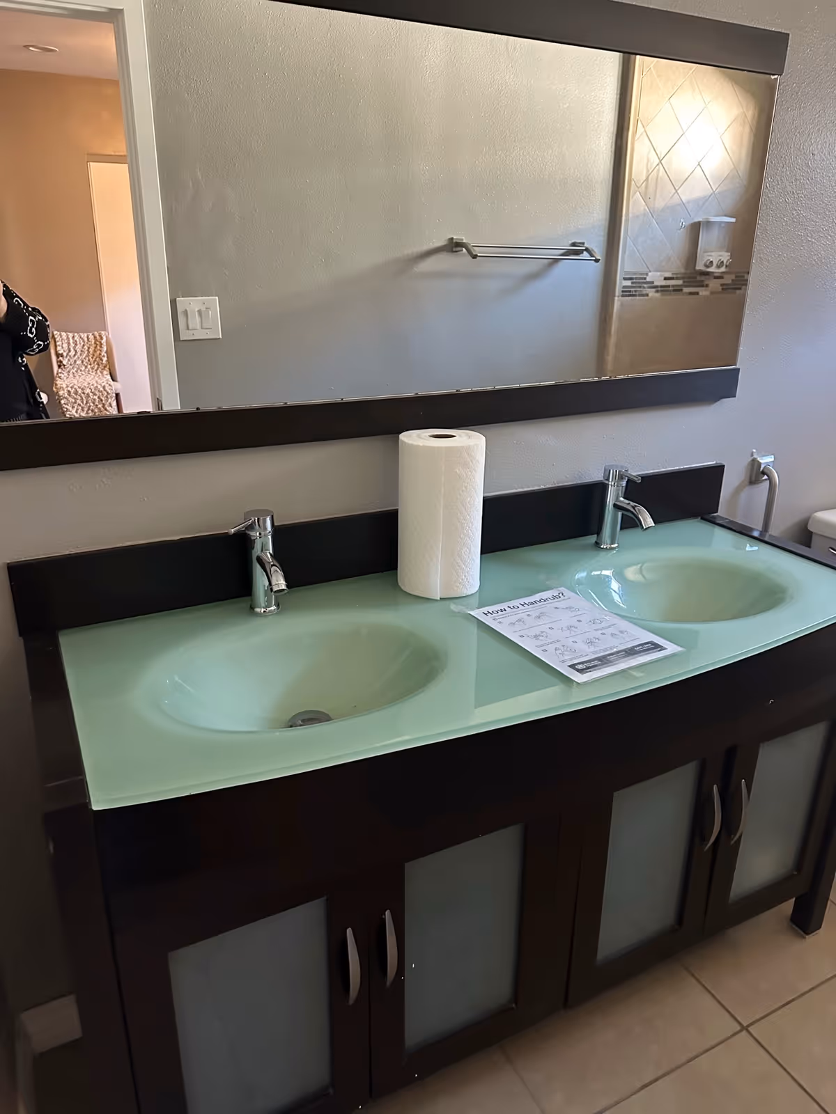 Double-sink bathroom vanity with frosted glass countertop, large mirror, and cabinets.