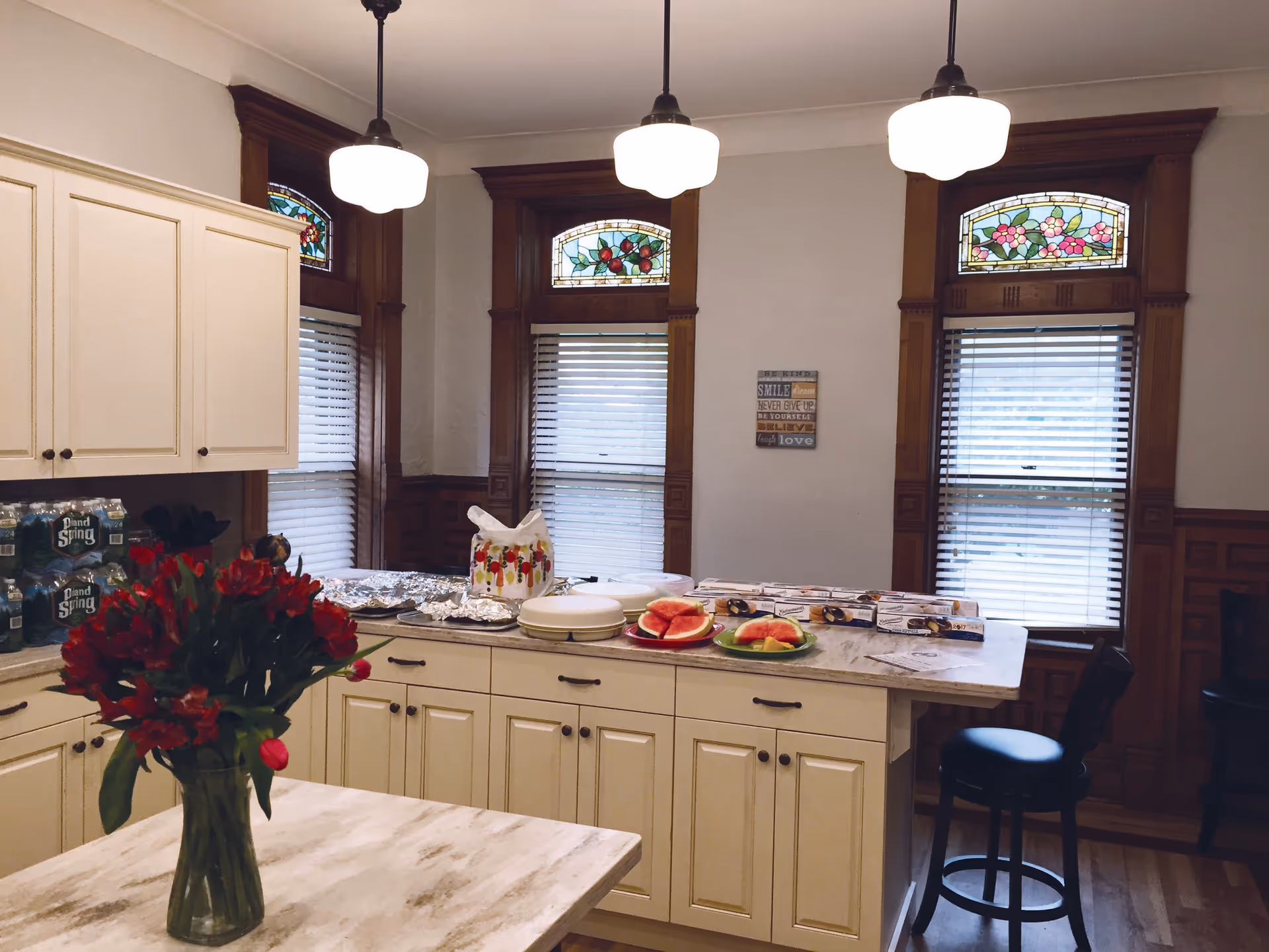 Bright kitchen with white cabinets, dark wood trim, and a vase of red flowers.
