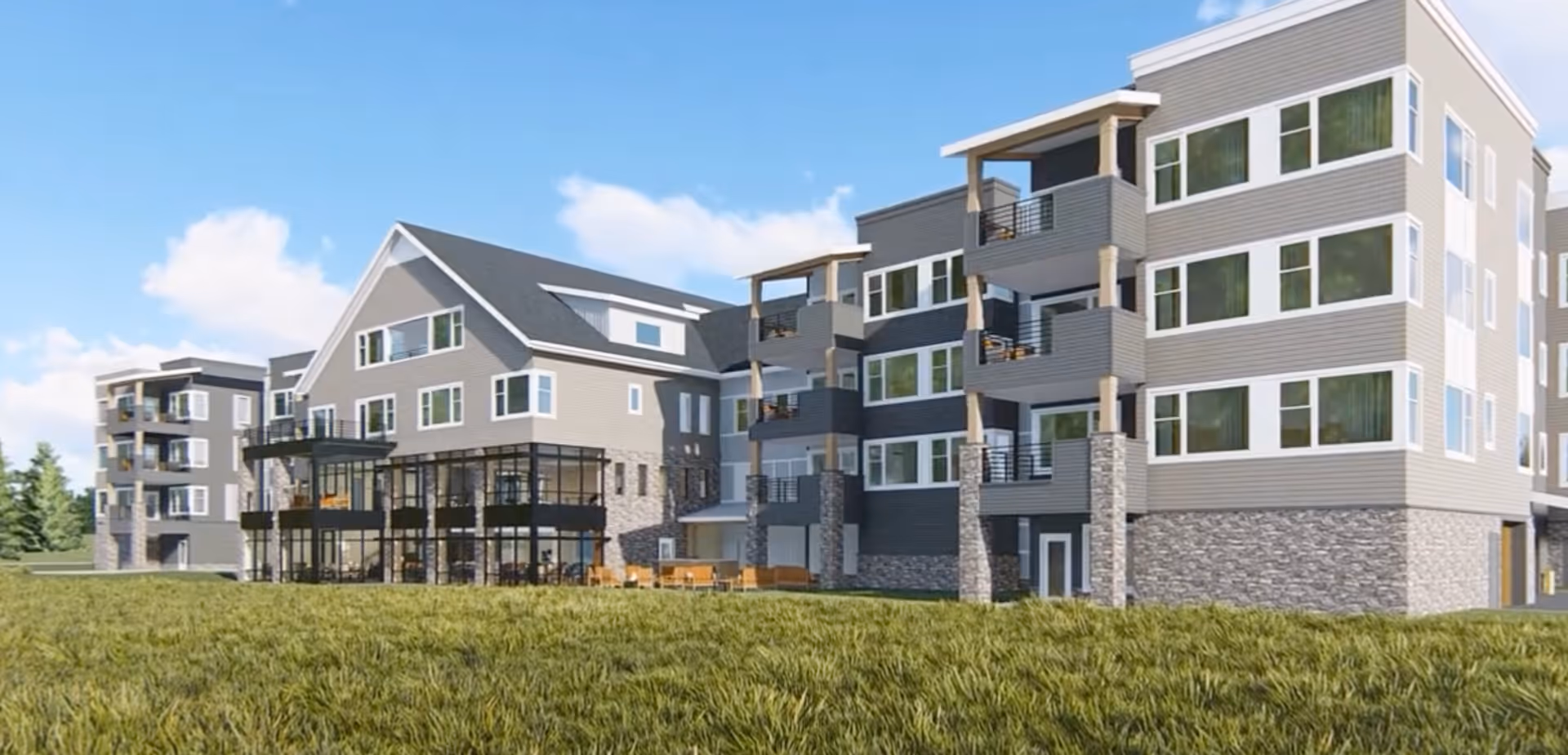 Exterior view of a modern multi-story senior living facility with balconies, large windows, and a stone and siding facade under a blue sky with some clouds. The building is surrounded by a grassy area.