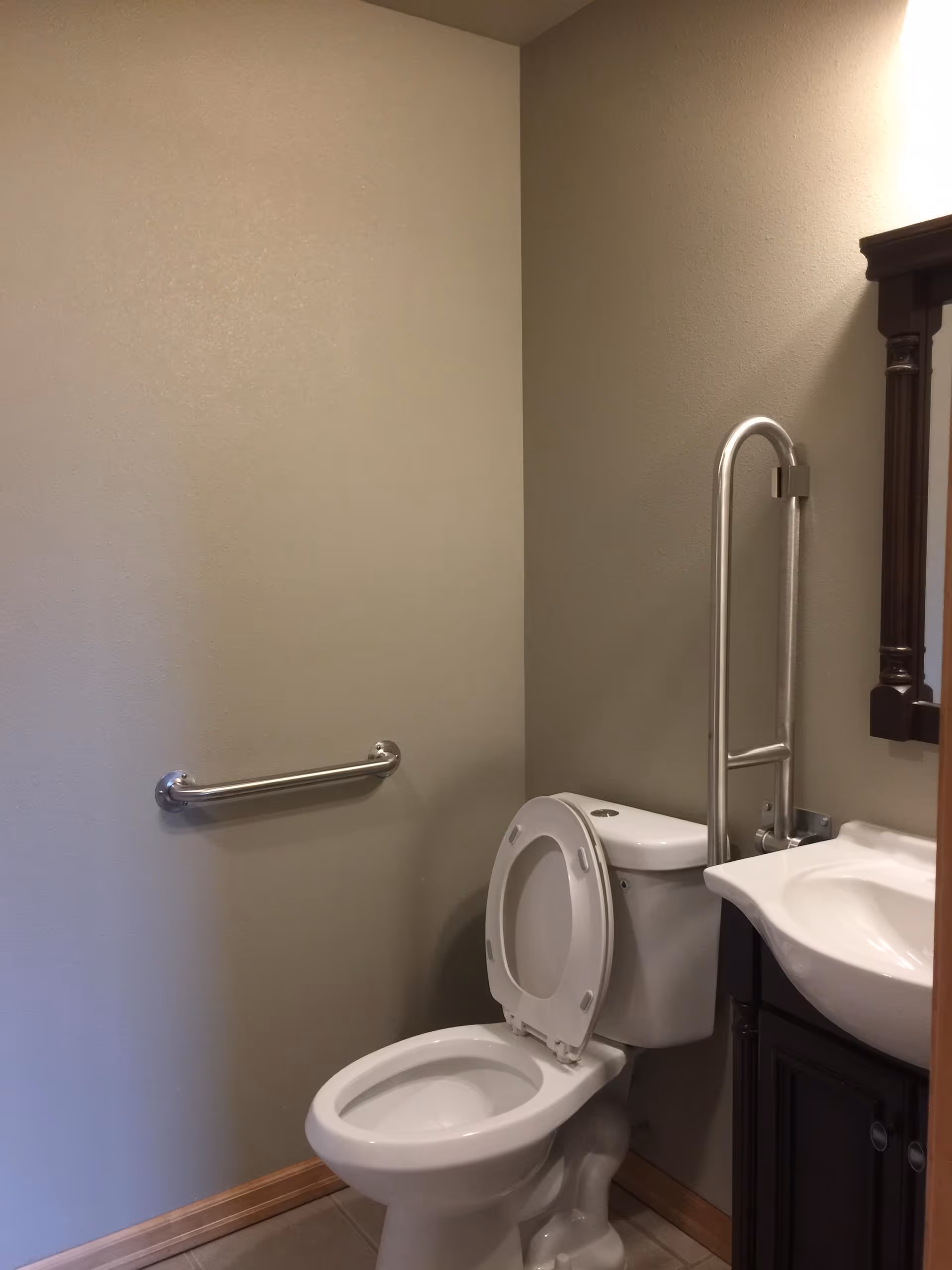 ADA-accessible bathroom with toilet, grab bar, sink, and mirror in a residential facility.