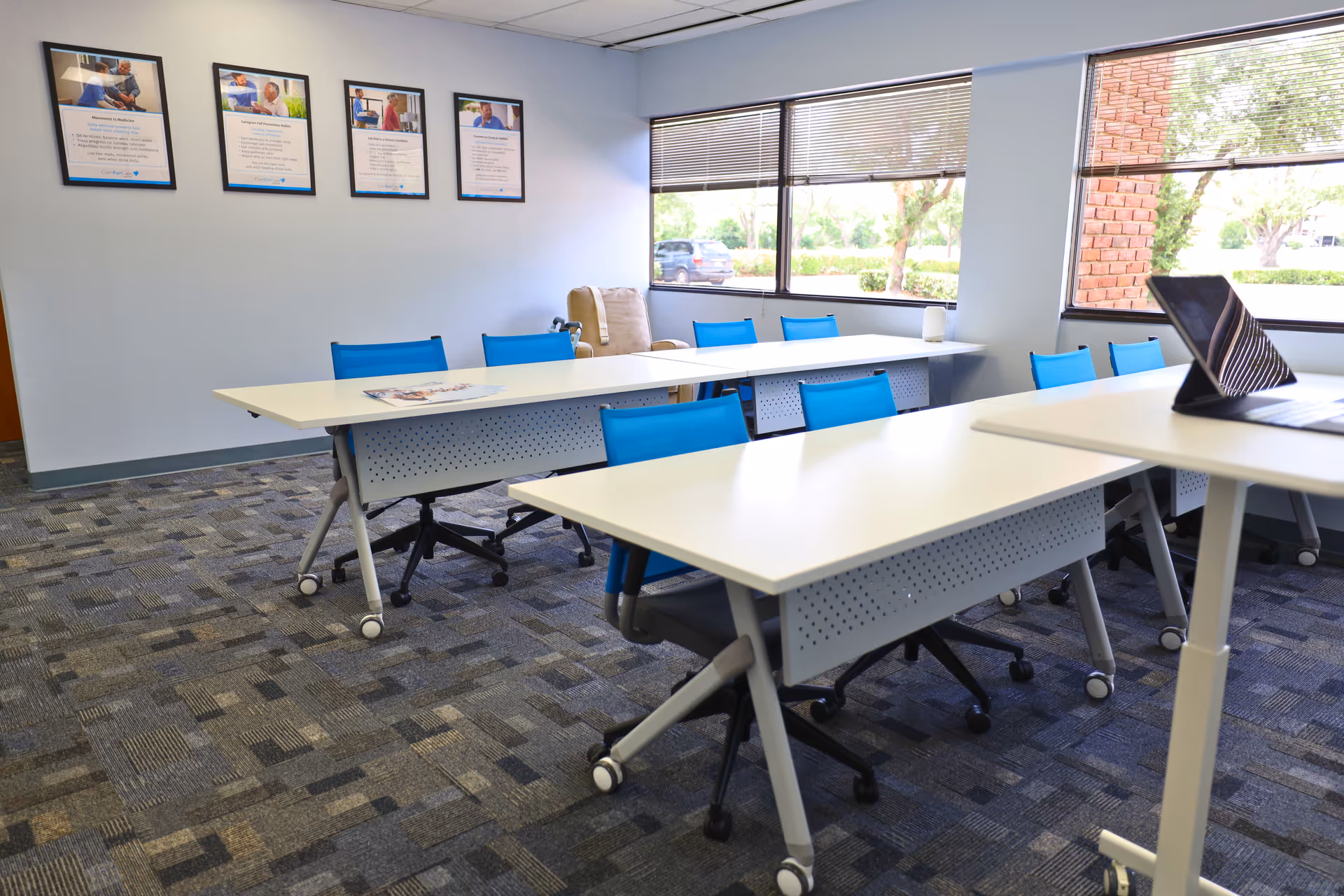 Interior meeting room with white tables, blue chairs, wall posters, and windows.