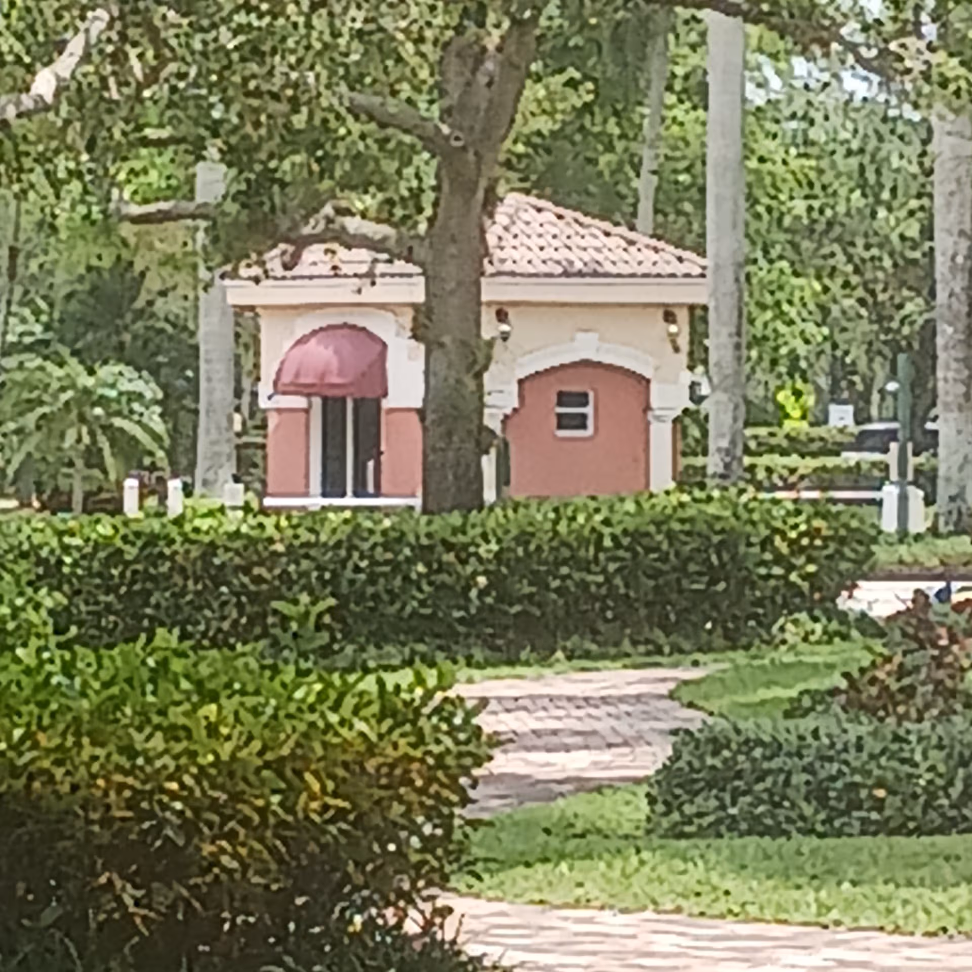 Small pink building with an arched doorway amid trees and hedges in a landscaped garden.