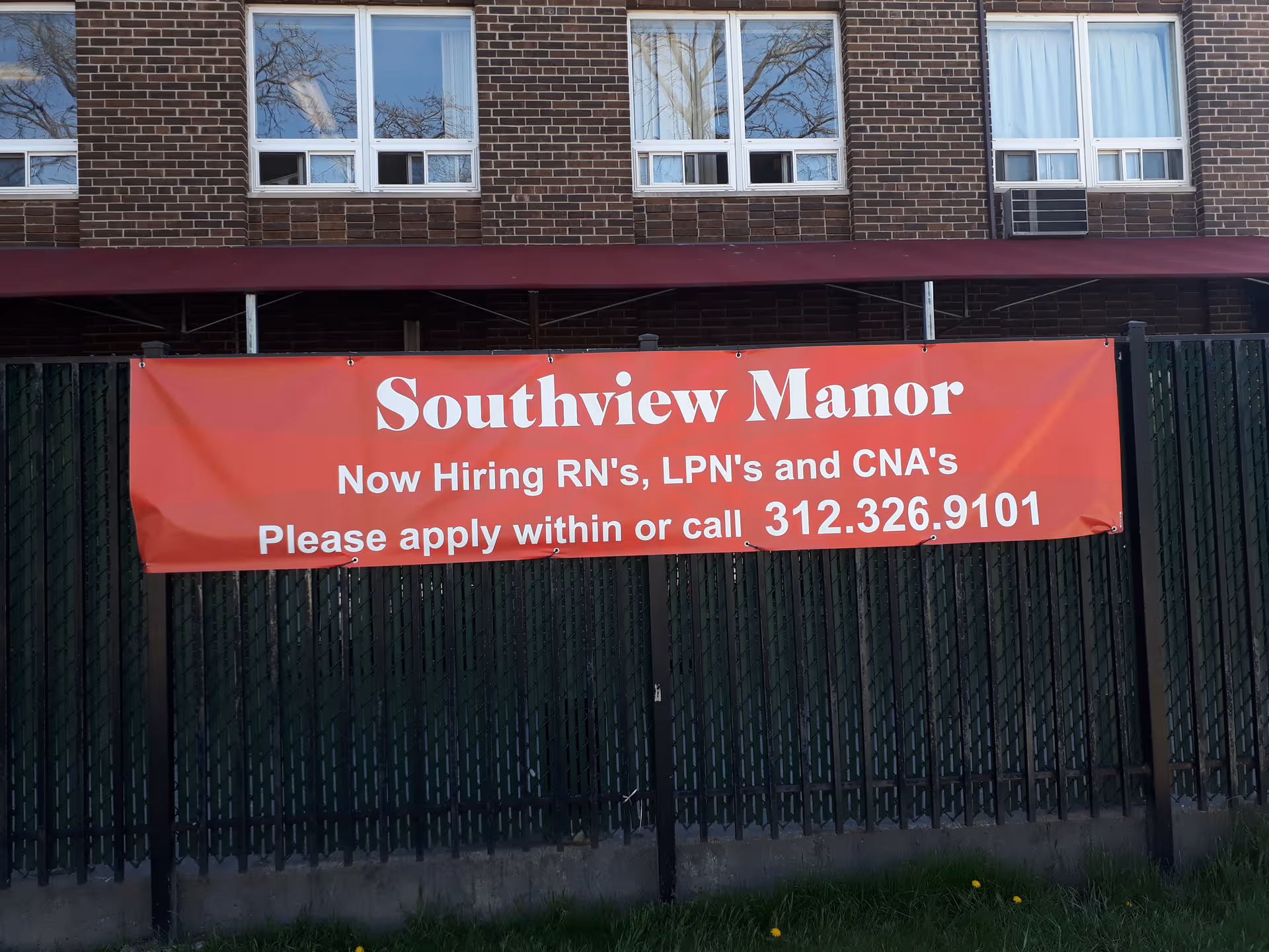Brick building with a large red banner advertising Southview Manor outside by a fence