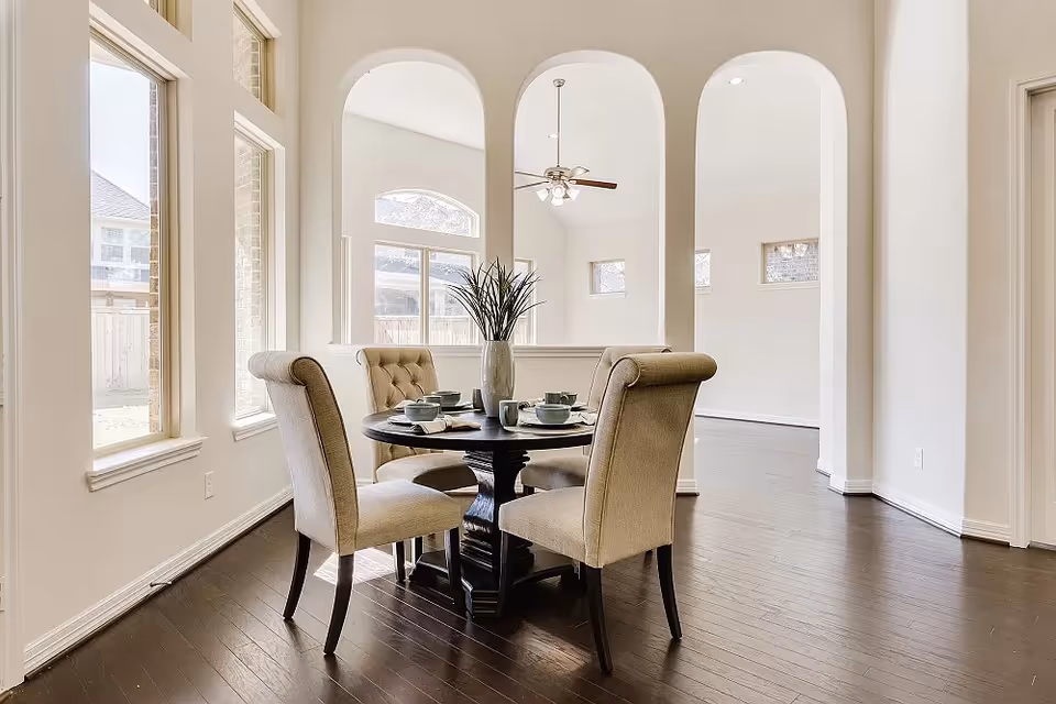 Dining room with round table, beige chairs, arched doorways, and dark hardwood floor.