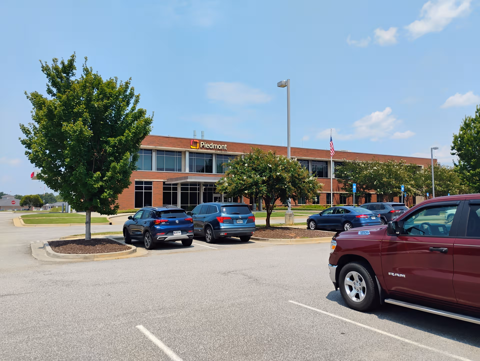 Exterior view of a two-story brick building with a Piedmont sign, trees, and parked cars.