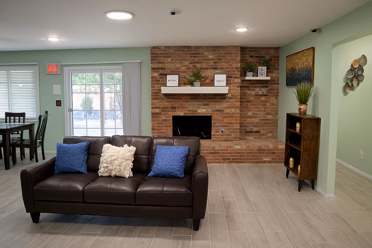 Modern senior living lounge with a brown leather sofa, brick fireplace, and decorative shelves.