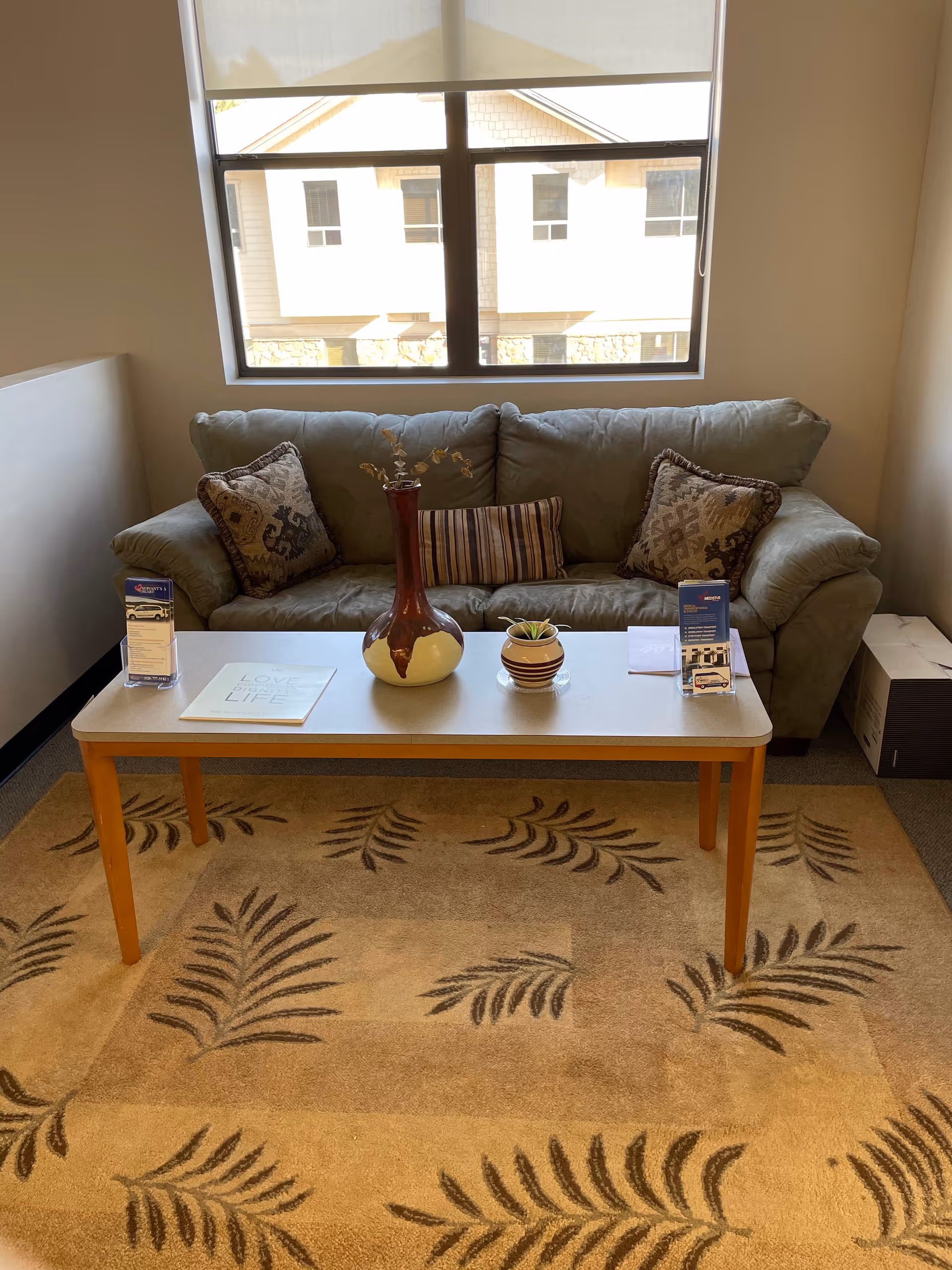 Cozy lounge area with sofa, coffee table, plants, and a leaf-patterned rug.
