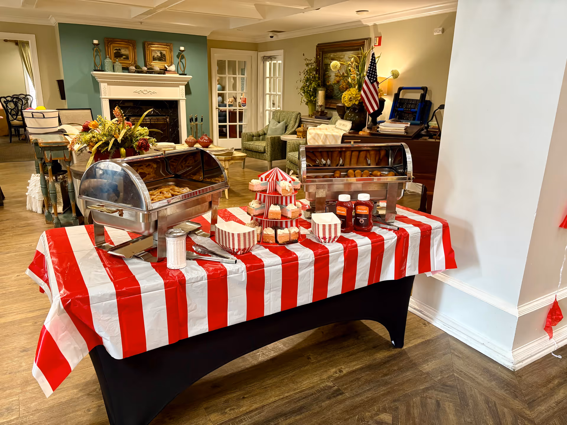 Buffet setup with chafing dishes on a red and white striped tablecloth in a senior lobby.