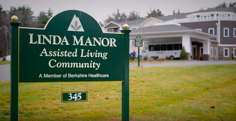 Green Linda Manor sign in foreground with assisted living facility entrance in background.