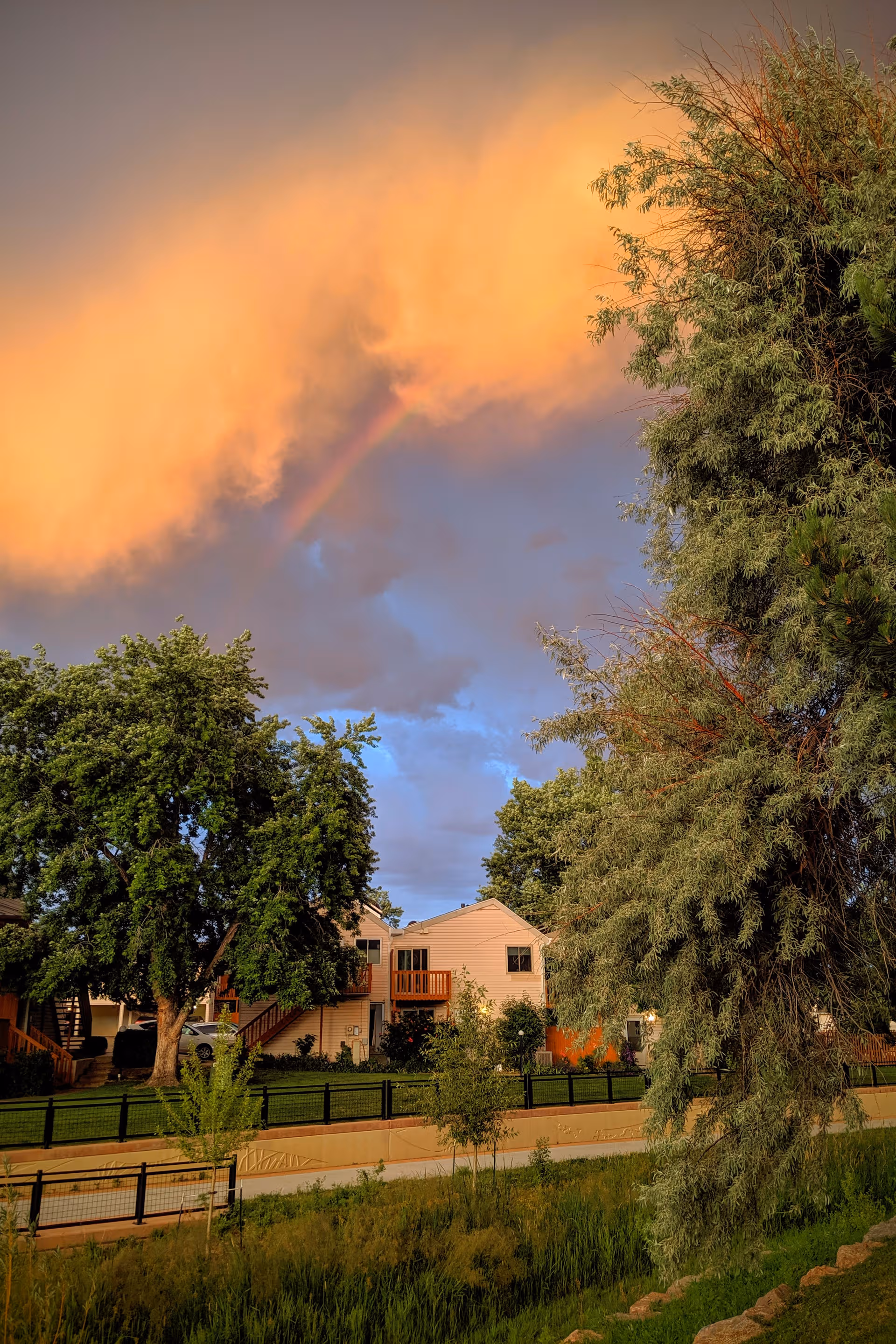 Exterior view of Brookdale Boulder Creek with trees, a fence, and rainbow over buildings
