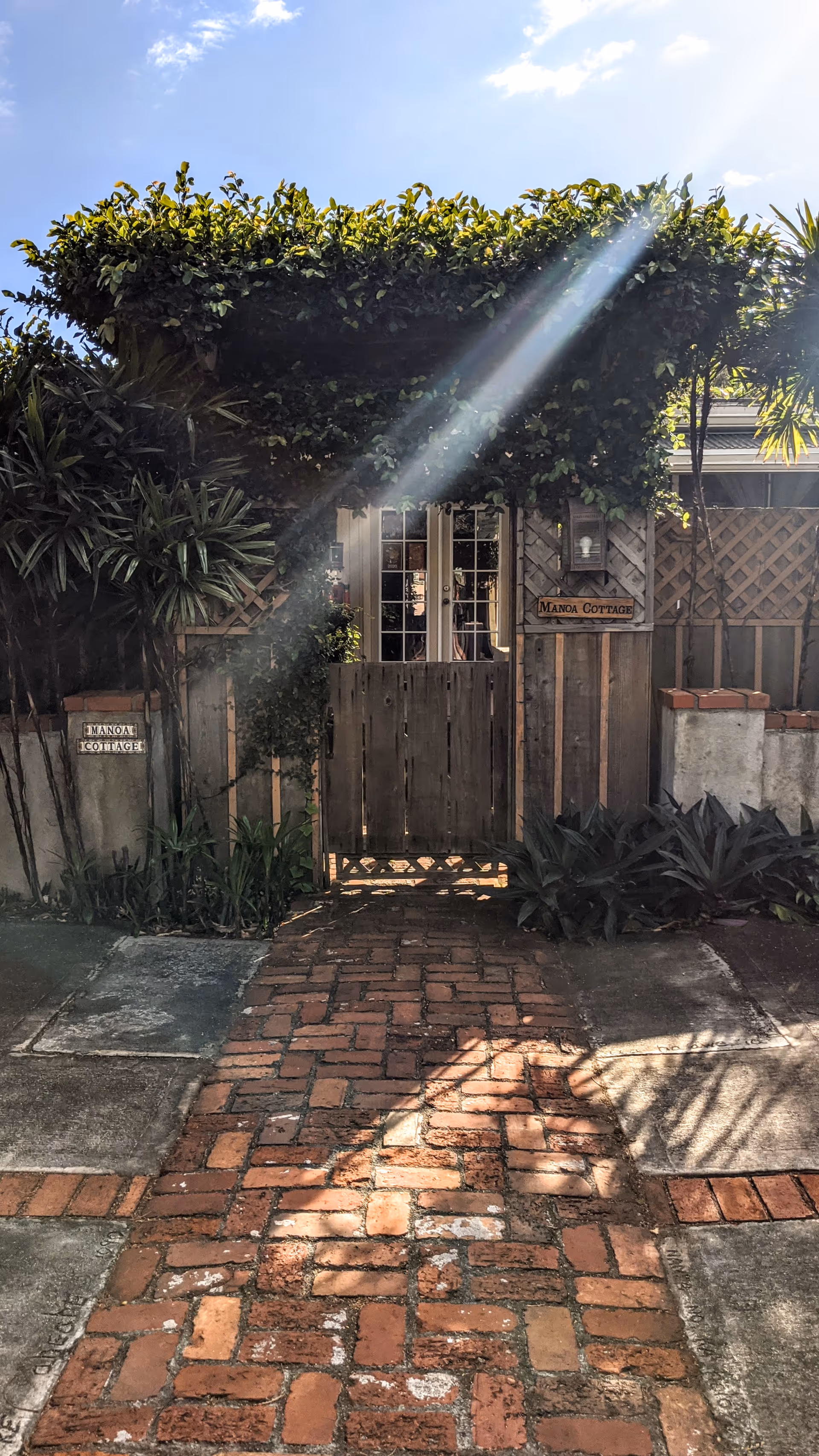 Wooden gate, brick path, and greenery lead to the Manoa Cottage entry.