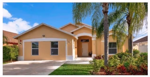 Single-story peach-colored senior living facility with a driveway and palm trees in front.