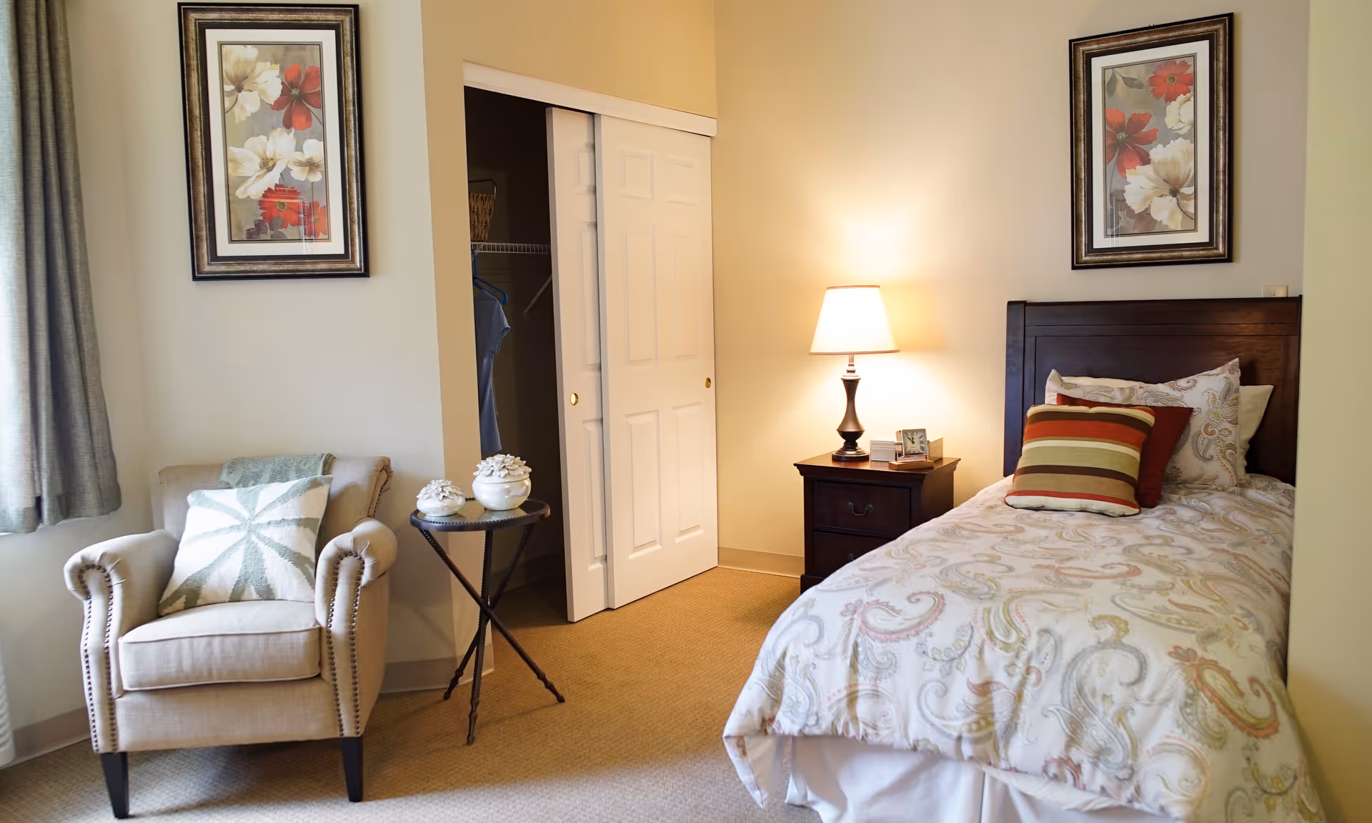 A cozy bedroom with a bed, armchair, nightstand, and closet in soft lighting.