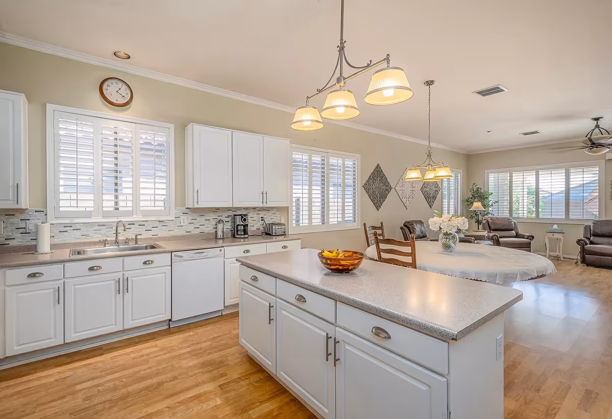Bright open kitchen with white cabinets, island, and adjacent dining/living area.