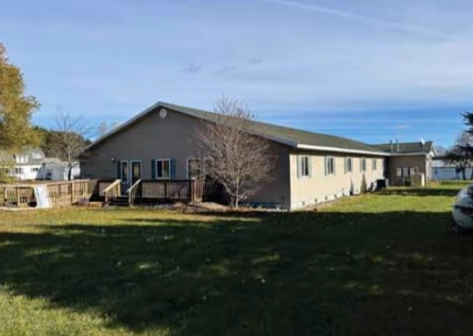 Exterior view of a single-story senior living facility with a deck and grassy yard.
