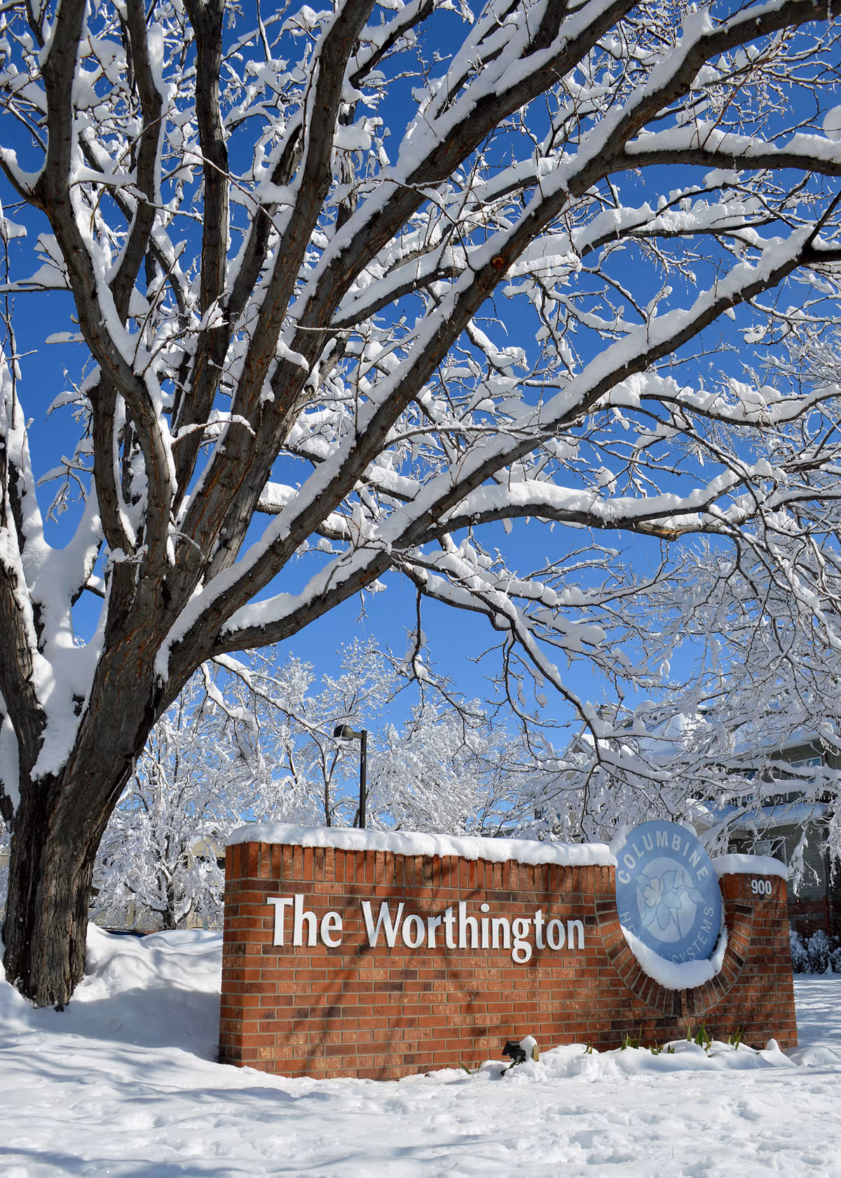 Snow-covered brick sign reading The Worthington beside the facility entrance.