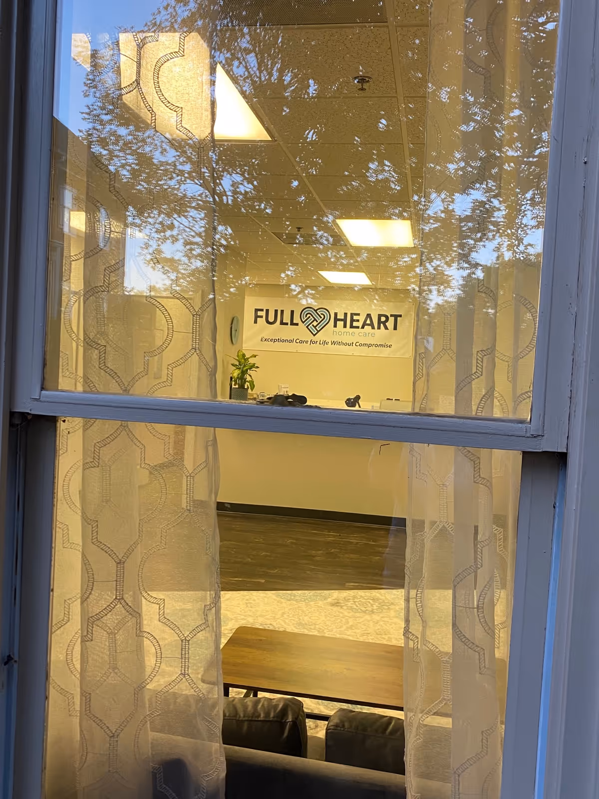 Interior view of a facility lobby through a window, featuring a Full Heart Home Care sign.