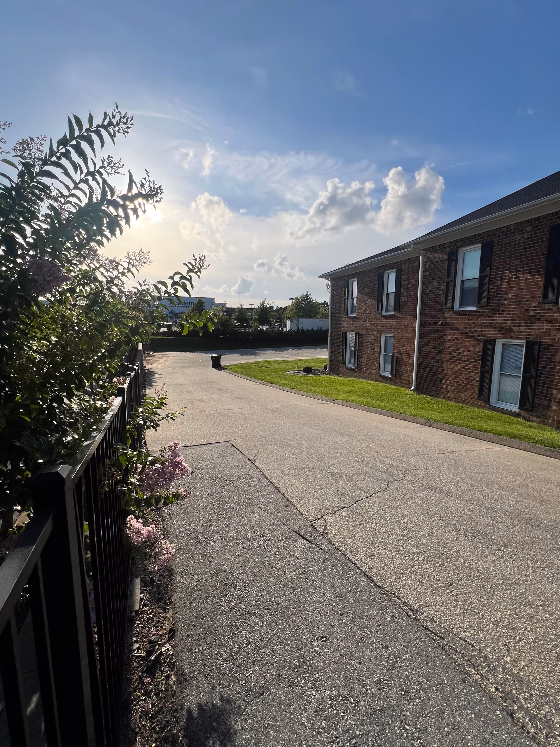 Brick senior living building on the right with a paved driveway and fence-lined greenery.