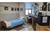 A small bedroom in a senior living facility with a single bed, desk, and dresser.